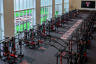Downward view of the Texas Tech Football weight room with a full view of squat racks and the view of the outdoor practice field.