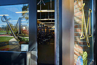 Doorway into the Millersville University Performance Center. The glass doors have the Millersville logo featured on the doors and a view of the performance center can be viewed. The space utilizes REGUPOL aktivpro roll flooring throughout the facility.