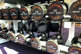 Clemson dumbbells on a rack in the Clemson weight lifting facility.