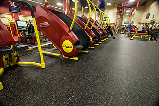 The stair machines at Retro Fitness Stroudsburg are themed red and yellow to match the brand colors and rests on REGUPOL aktiv.