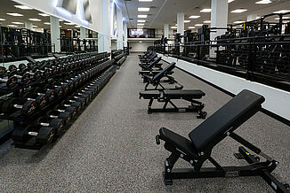 University of Texas at Austin Weight Training - Free Weight Area View of the dumbbell rack and benches offered to the free weight section of the University of Texas at Austin athletic weight training facility. The equipment is positioning on REGUPOL aktivpro roll flooring.