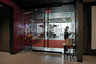 Glass doors leading into a brightly lit fitness center with cardio equipment.