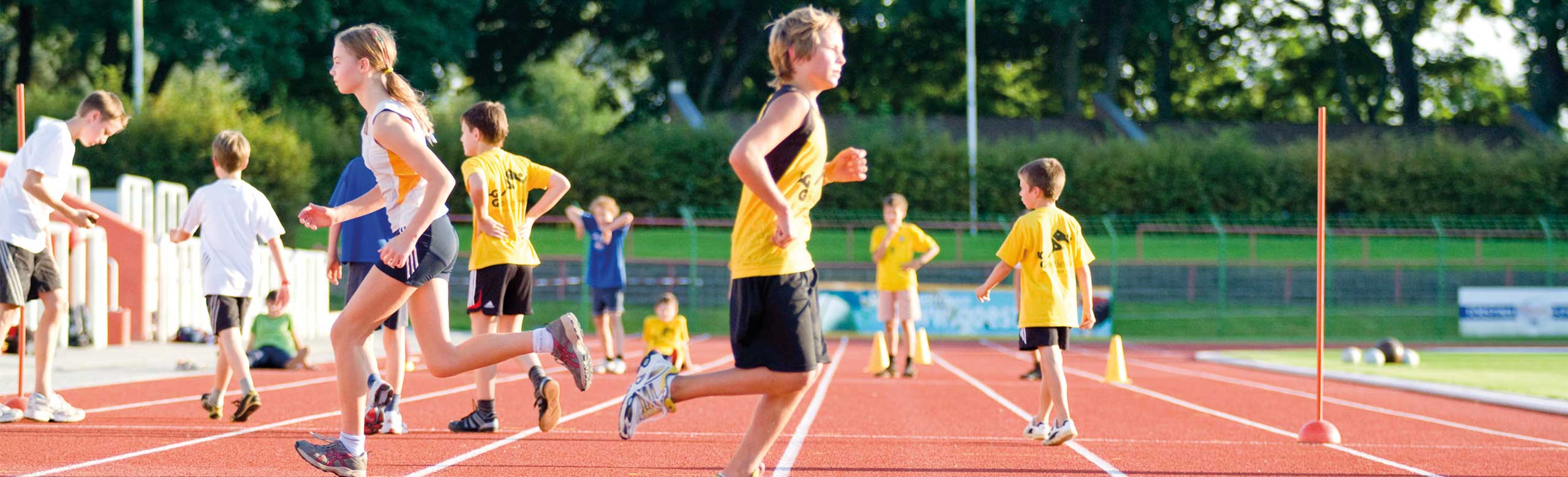Children on REGUPOL track during training or playing. Children and young athletes running and playing on a red synthetic track under sunny skies at the stadium.