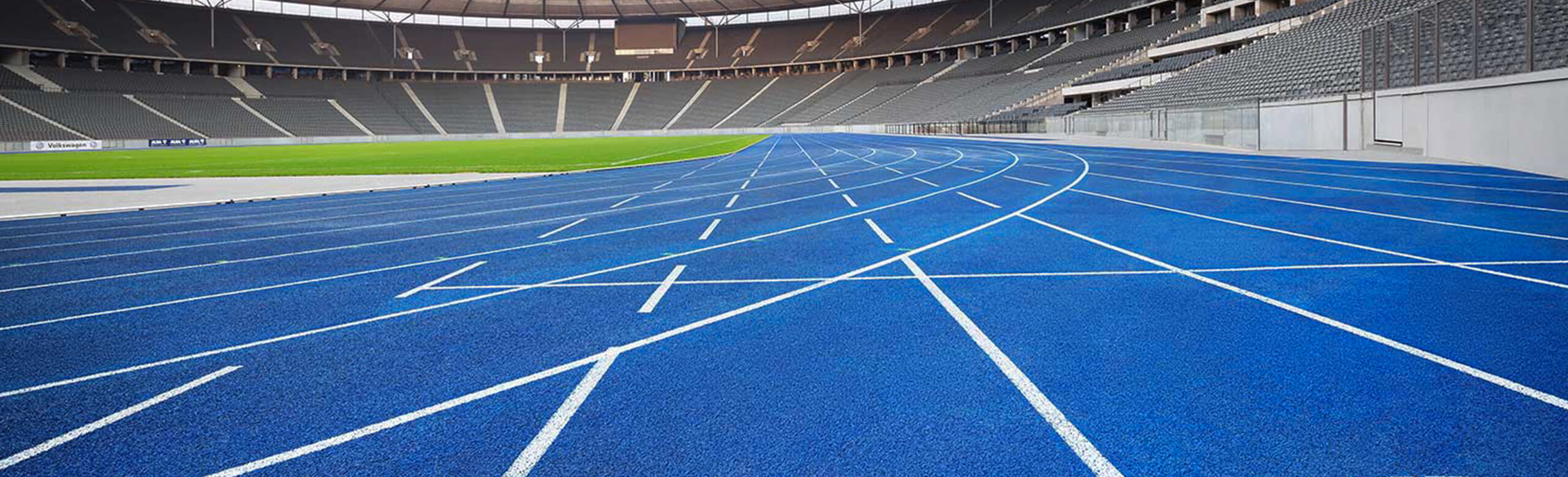 The blue synthetic running track at Berlin Olympic Stadium, known as “the Blue Miracle.” Curved lanes in front of empty stands represent a modern athletics surface in a world-class track and field venue.