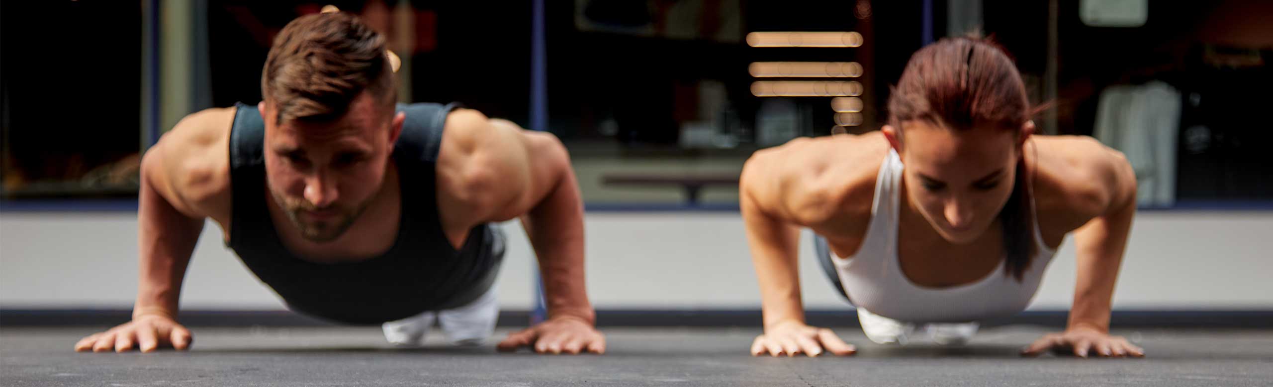 REGUPOL aktiv floors can be utilized for a variety of exercise types, including functional training. The image shows a man and a woman performing push ups on REGUPOL flooring.