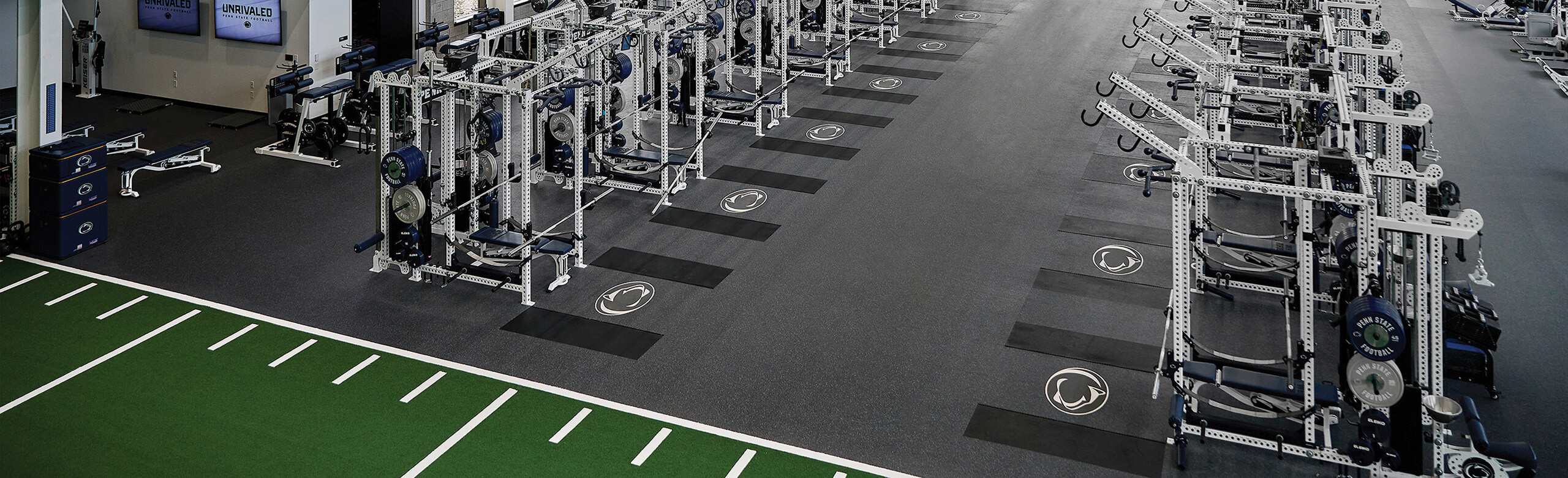 Penn State University's Football Weight Room Overhead view of Penn State's football weight room with weight racks, benches, and turf area, showcasing the Penn State logo within REGUPOL aktivpro roll flooring and crash zones.