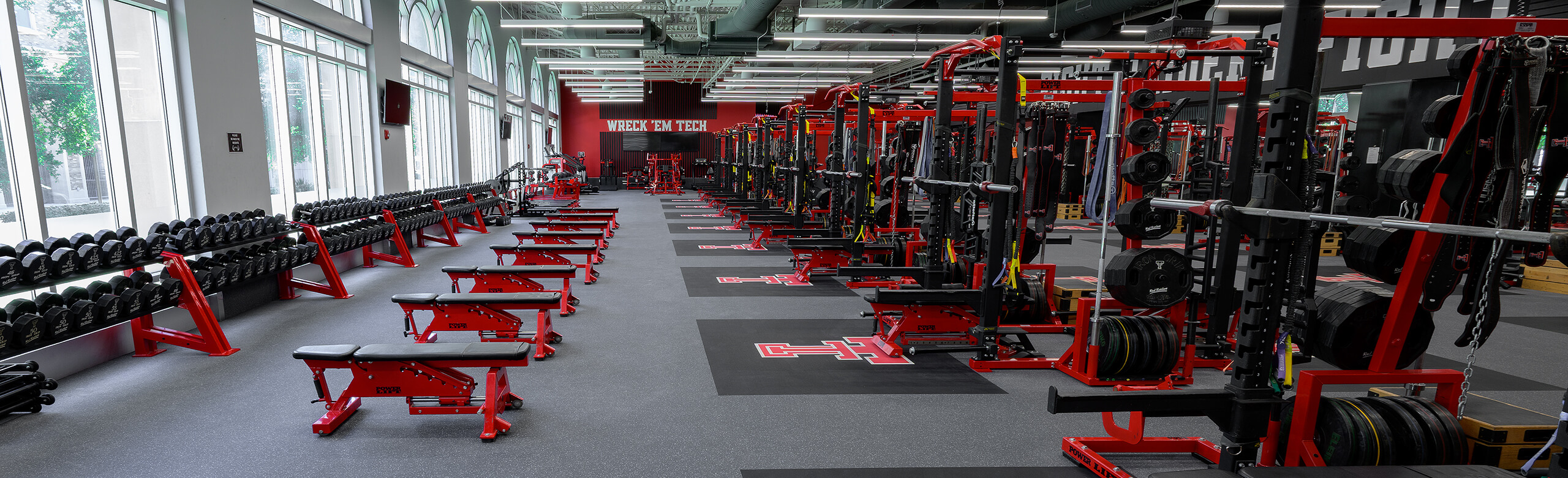 View of the side of the Texas Tech Olympic room that features free weights and benches, as well as weight racks.